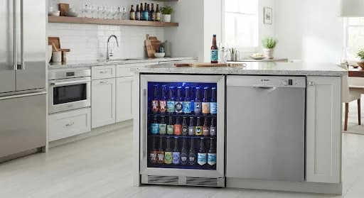 Cervejeira embutida em bancada de cozinha moderna, com porta de vidro e iluminação interna azul destacando as garrafas geladas