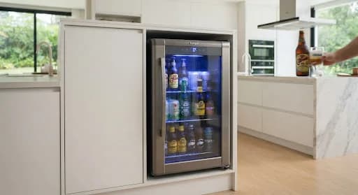 Cervejeira de aço com porta de vidro e iluminação interna azul instalada em cozinha clara